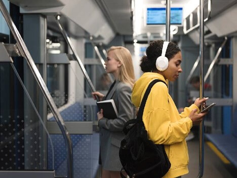 دختر جوان در مترو در حال یادگیری زبان انگلیسی با فایل‌های صوتی با امکان توقف پادکست است.